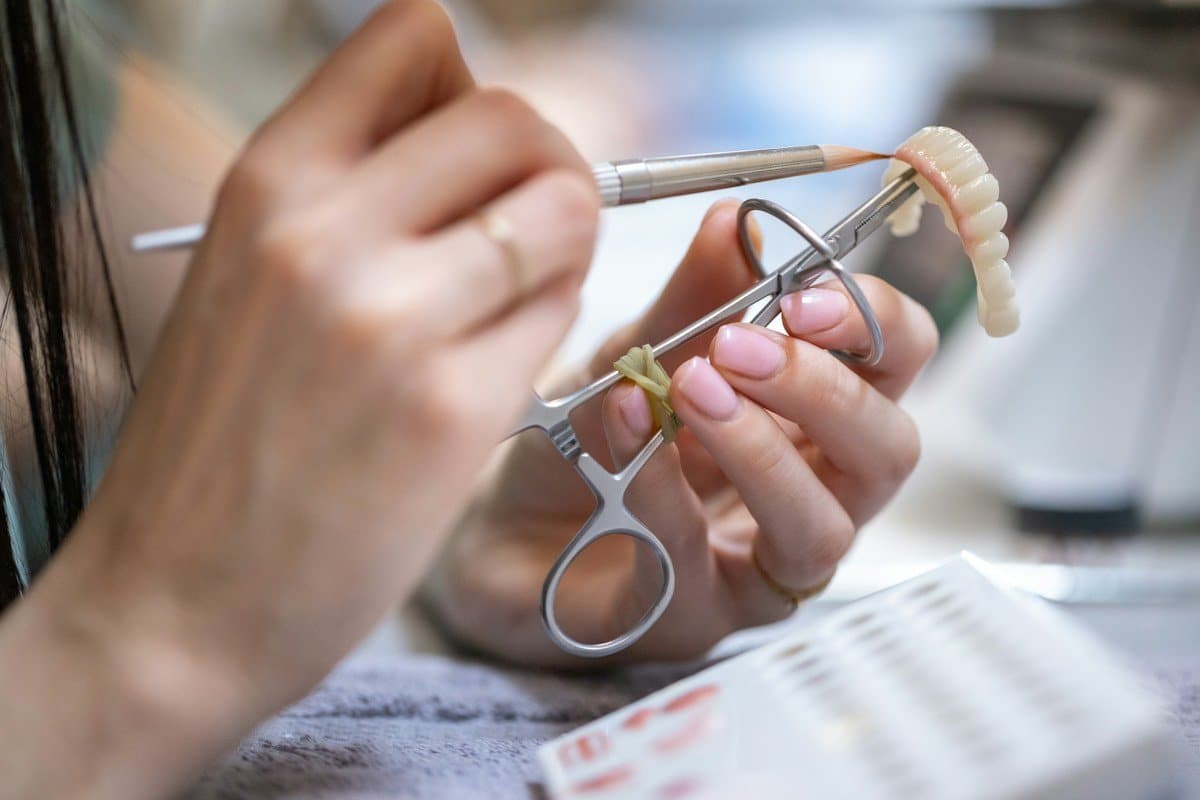 Hands painting shade onto a porcelain dental restoration in a lab