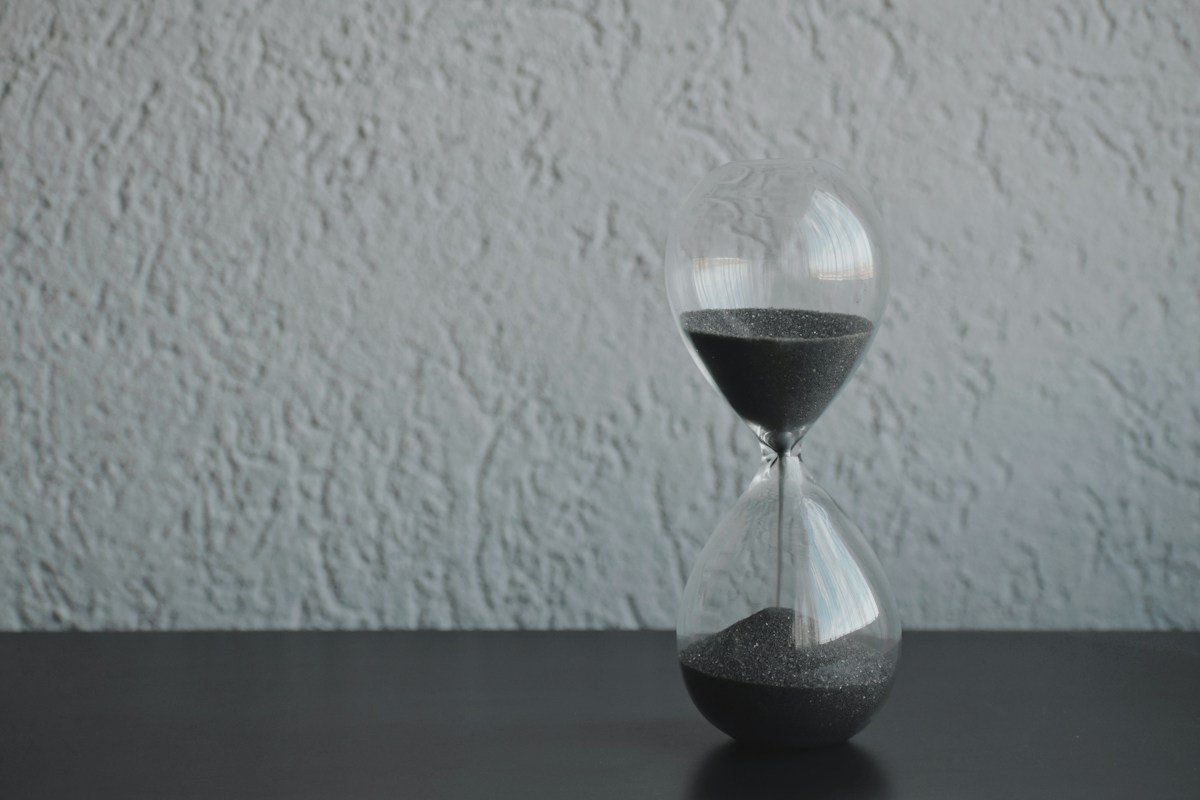 Glass hourglass with dark sand on a table, a reminder that veneers age over time
