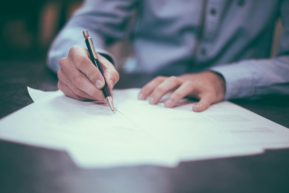 Hands holding a pen over printed paperwork on a desk